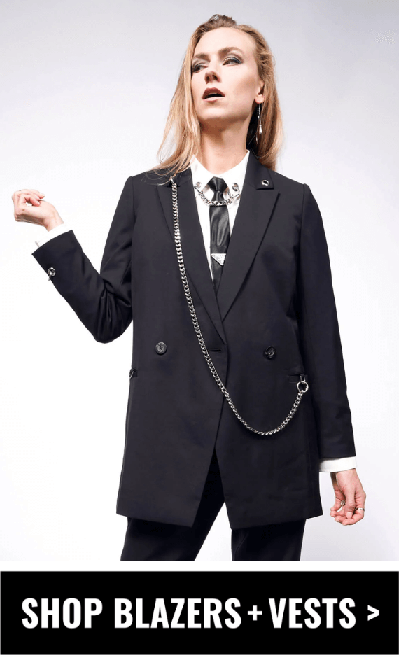 Person with long blonde hair wears The Debbie Harry x Wildfang Double Breasted Blazer with The Debbie Harry x Wildfang Long Sleeve Button Up in white underneath on light background. Button underneath image says SHOP BLAZERS + VESTS.