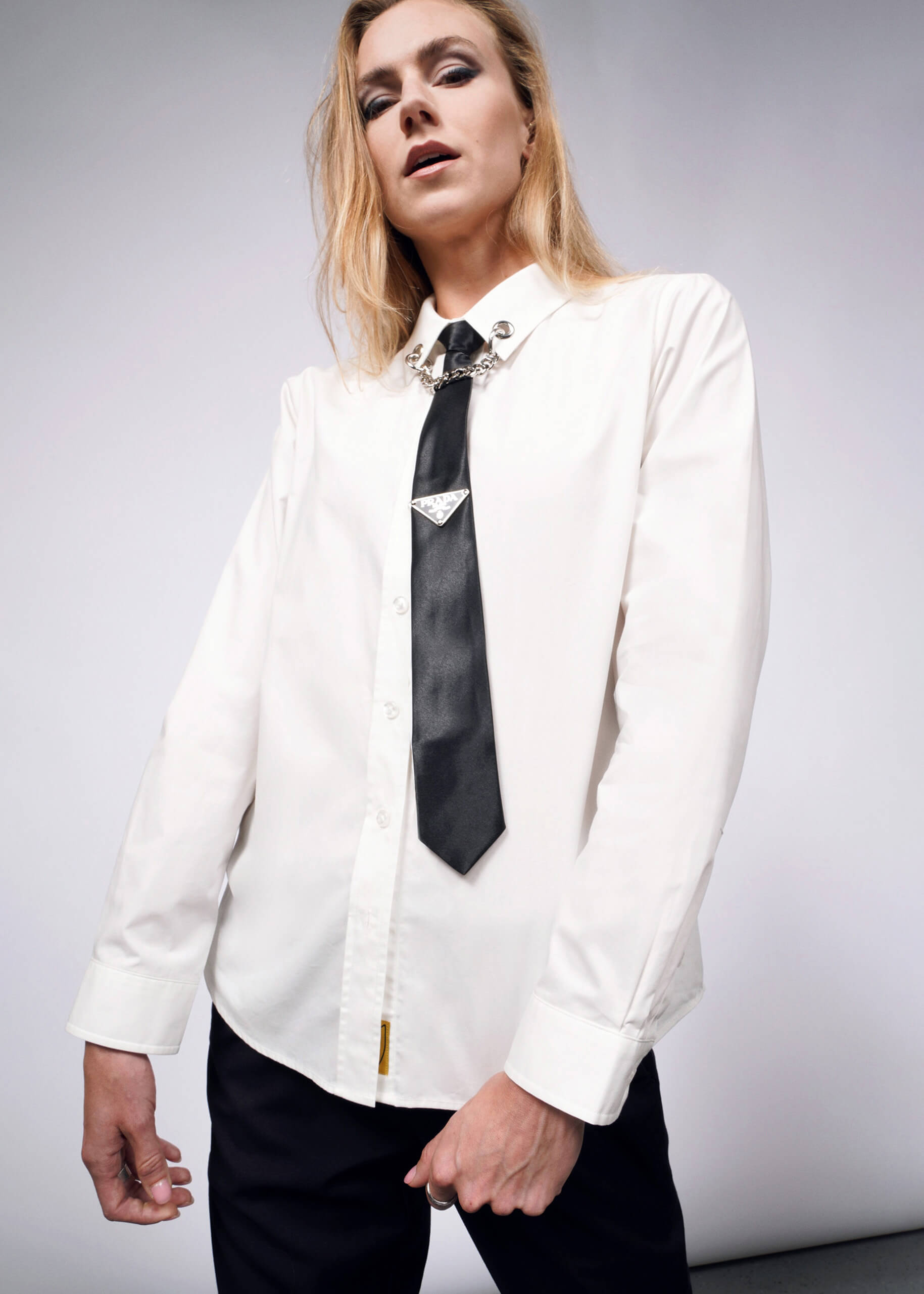 Sporting the Debbie Harry X Wildfang Long Sleeve Button Up and a black tie with removable chain detail, a person with long hair exudes punk aesthetics while confidently posing against a plain background.