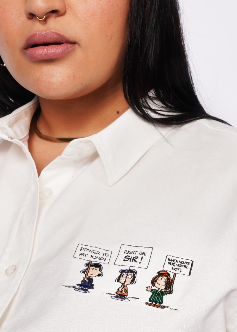 Close up of person wearing white button up shirt showing detail of embroidered Peanuts characters.