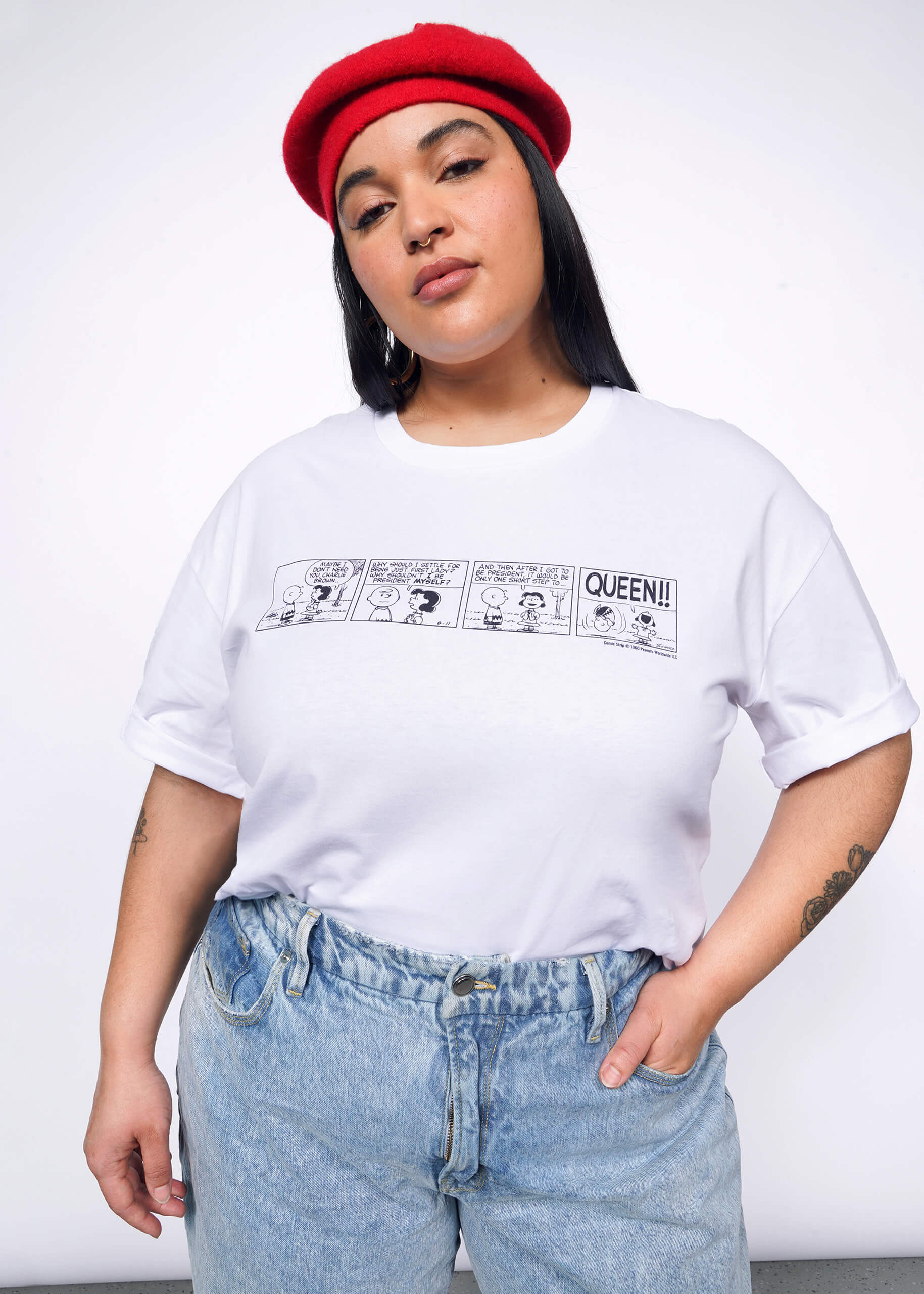 Person with long black hair wears tshirt with Peanuts comic strip printed on it, a red beret, and jeans.