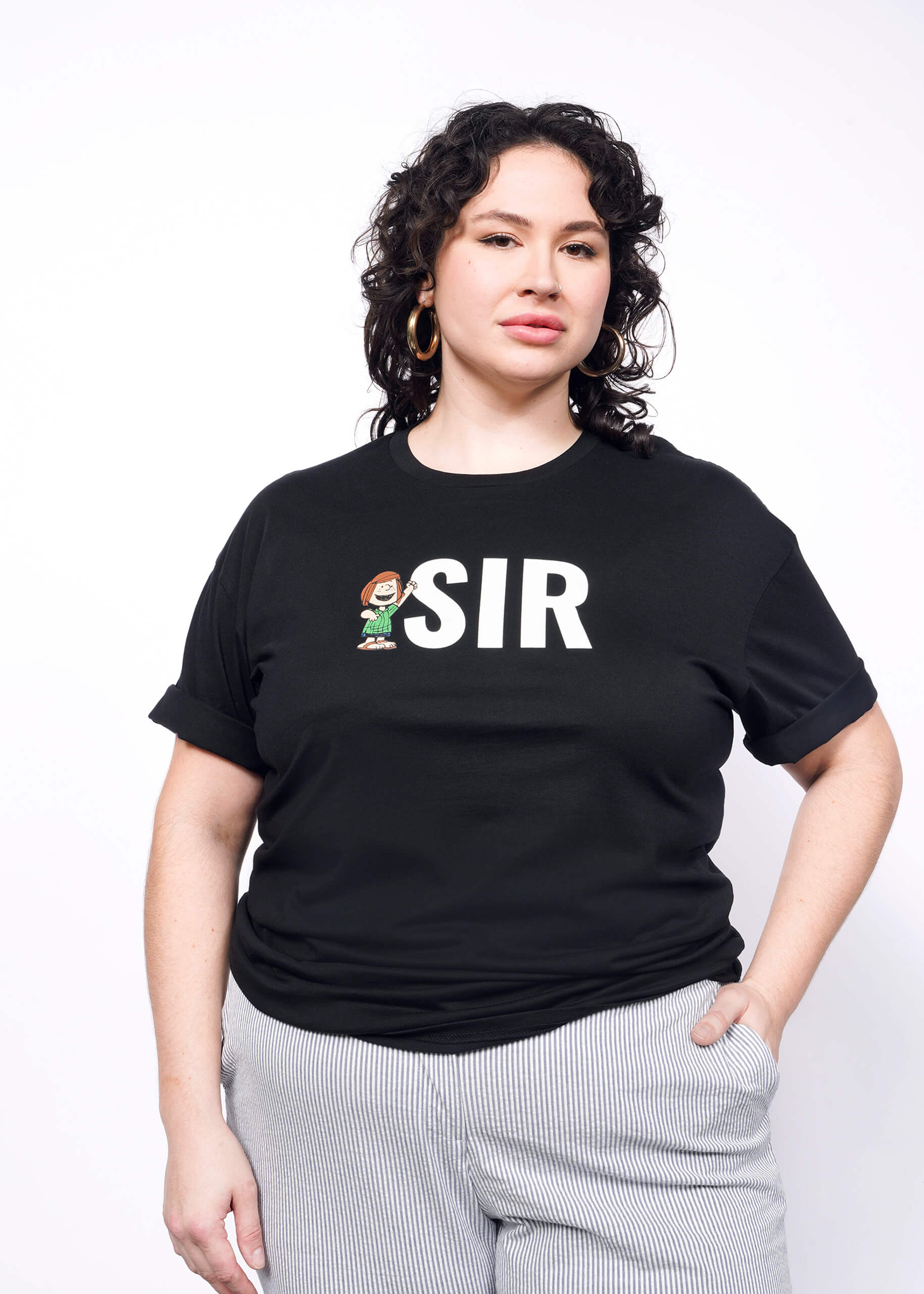 Person with short curly black hair wearing hoop earrings, seersucker trousers, and black tshirt with "SIR" and Peppermint Patty printed on it.