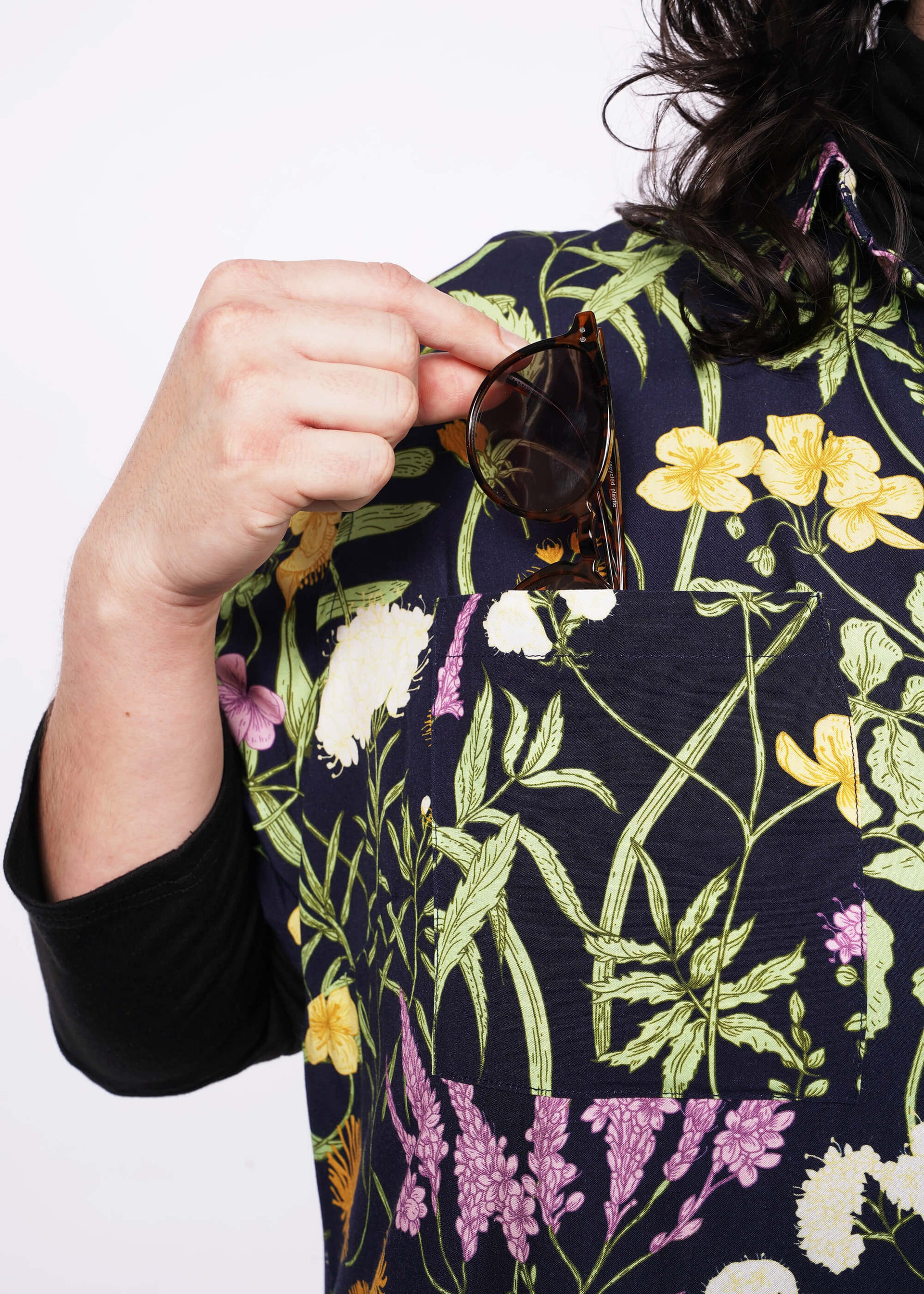 Close up view of person putting sunglasses in front pocket of botanical printed shirt dress.