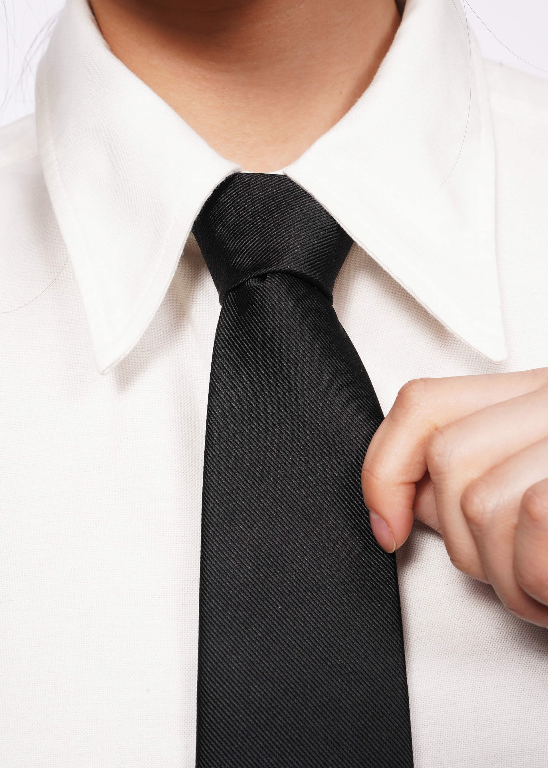 Close up of black tie on white shirt with model's hand holding tie.