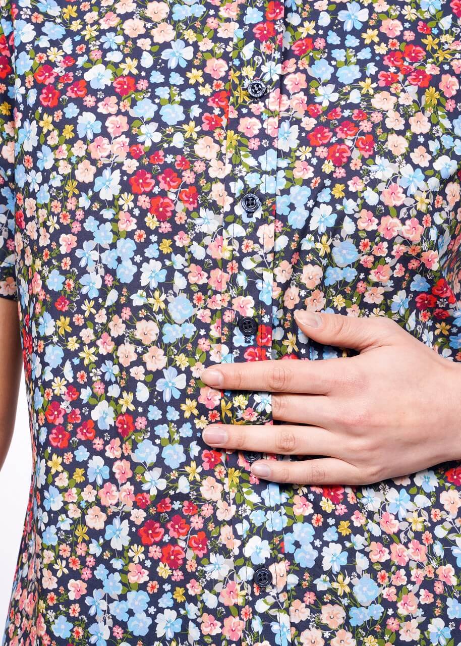 Close up of buttons on floral printed button up shirt showing models hand in between button holes.