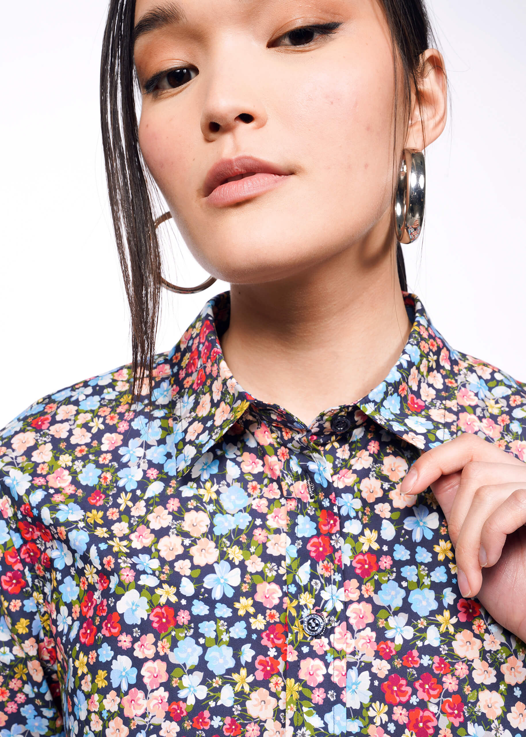 Close up of person with black hair tied back holding collar of flower printed button up shirt.