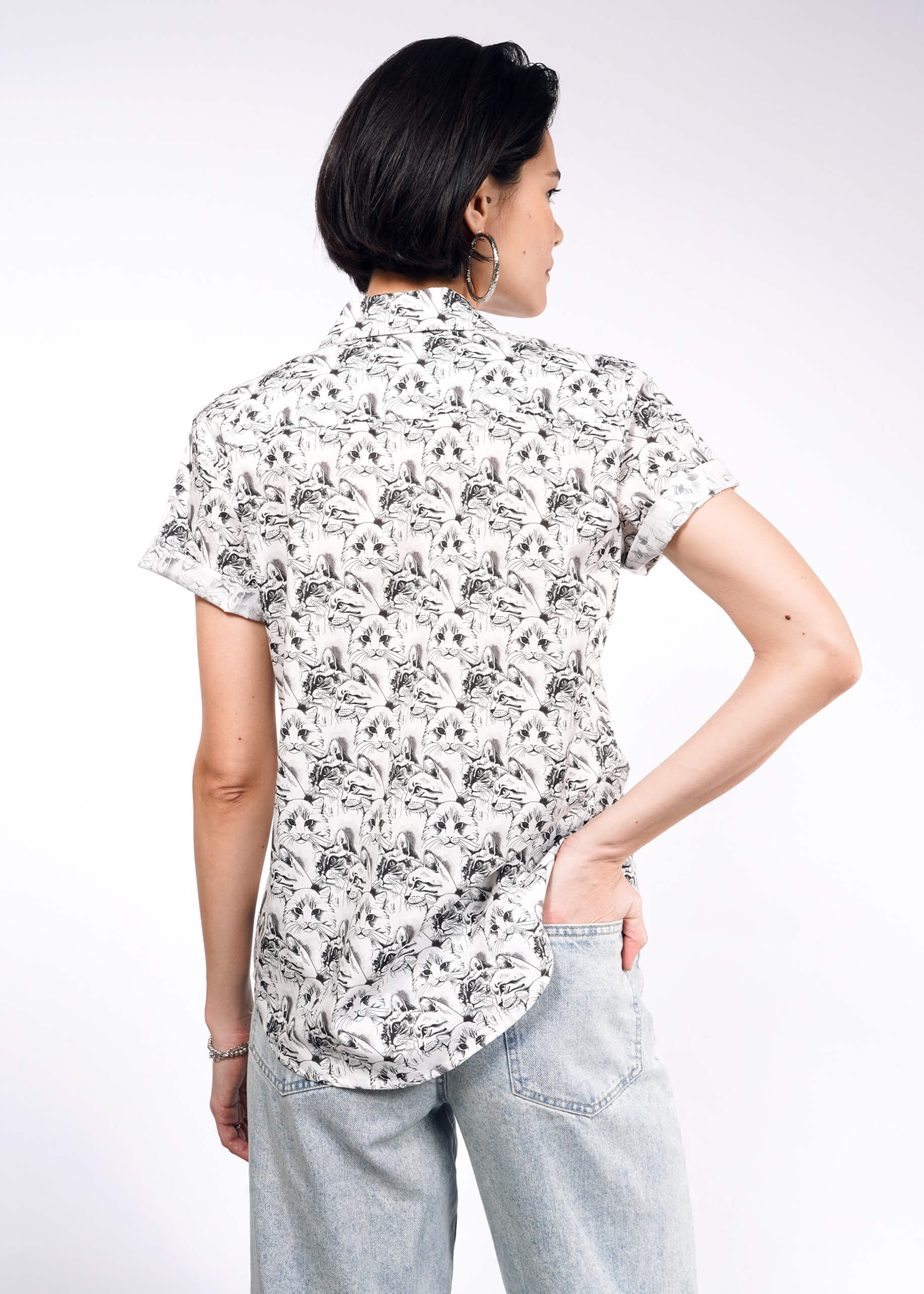 A person with short dark hair faces away, displaying The Essential Button Up—tailored with bold prints and Wildfang branded buttons—and light blue jeans against a plain white background.